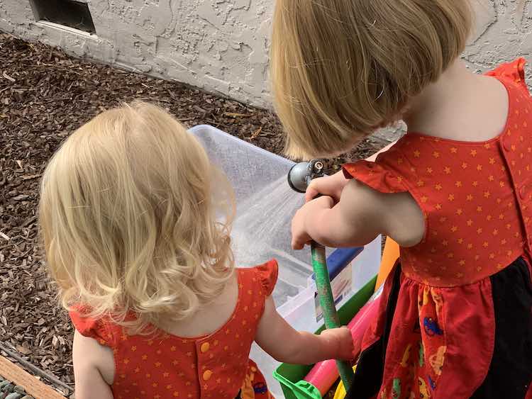 Ada and Zoey filling a storage bin with water.