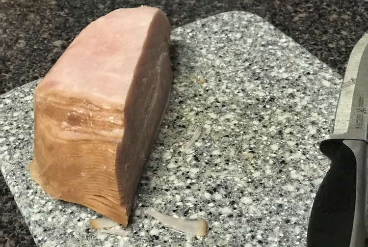 Closeup of a half stack of deli meat sitting on a marbled square cutting board with a knife next to it.