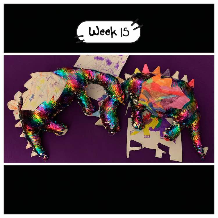 Image with the girls finished dinosaur dragon pillows. The pillows are facing each other and the one's head is resting on the other's neck. Under each pillow is the coloring page that came with the pattern that the kids and I used to plan them out.