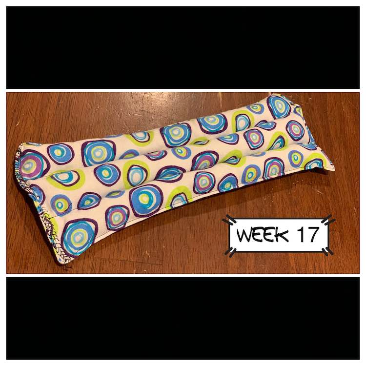 The finished eye pillow. It's made of white fabric with colored circles on it. The pillow is a long rectangle with three horizontal channels filled with rice. 