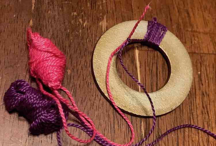 A swatch of purple embroidery floss on the washer. The purple floss is then tied to the pink embroidery floss with an excess pink thread end.