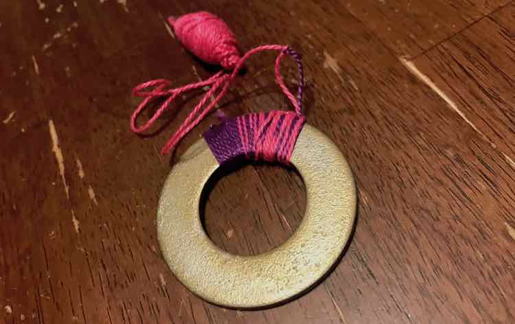 A washer with a second of purple and then a section containing both pink and purple. The thread coming from the washer is knotted and the excess purple is trimmed off.