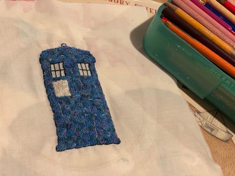 Finished TARDIS laid out with an open container of pencil crayons beside it.