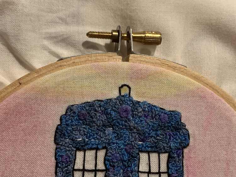Closeup of the top of the embroidery hoop showing the top of the TARDIS, the yellow rays extending outward, and the top closure of the hoop.