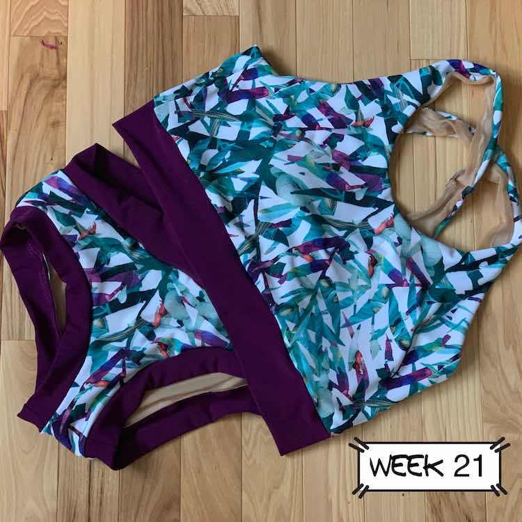 Front of the swimming suit with the top slightly overlapping the top corner of the swim bottoms. Main fabric is white with teal and purple leaves. The bands are all eggplant to match the purple in the main fabric. 