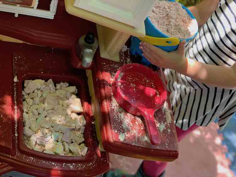 Kitchen set showing a sink full of chunks of oobleck while a blue sand pail sits full of oobleck sand.