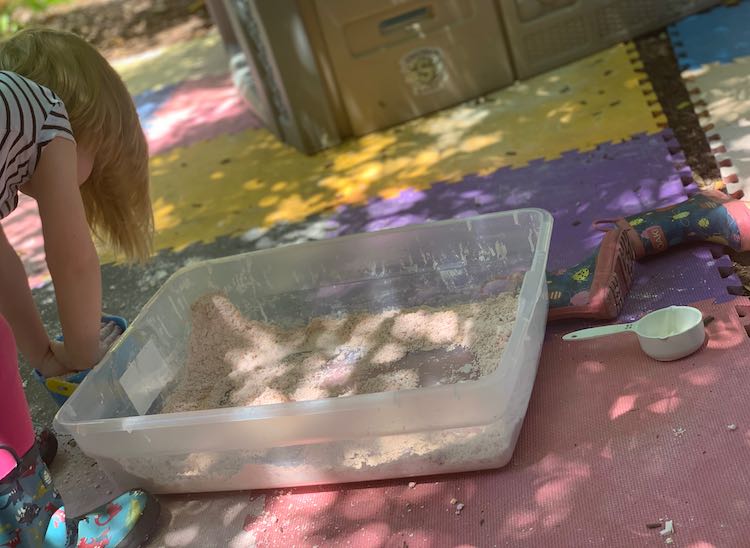 Ada flattening the pail of oobleck sand before dumping it into the bin sitting next to her.