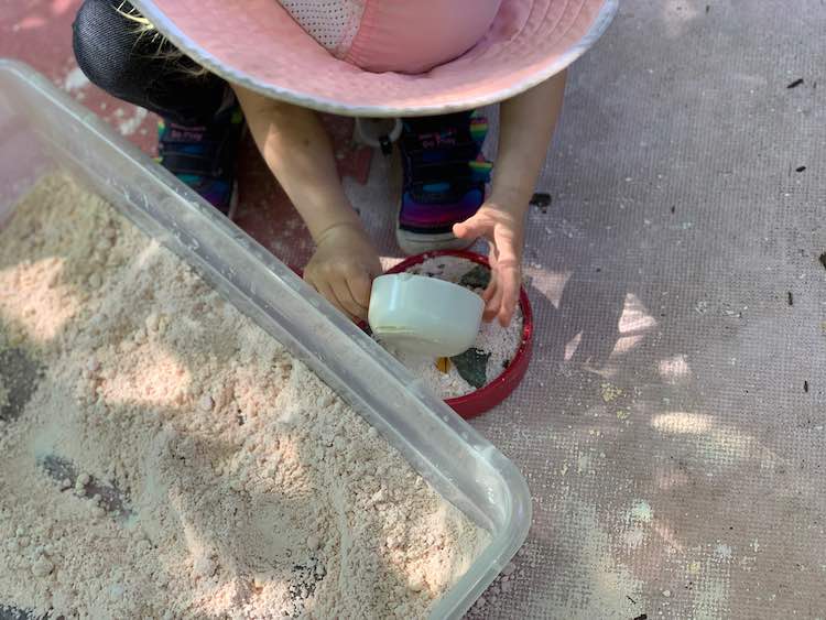 A pot of oobleck sand, rocks, and leaves getting topped off by more oobleck sand.