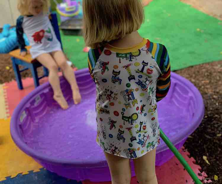 Ada filling up the swimming pool with the garden hose as Zoey puts her toes in the water.