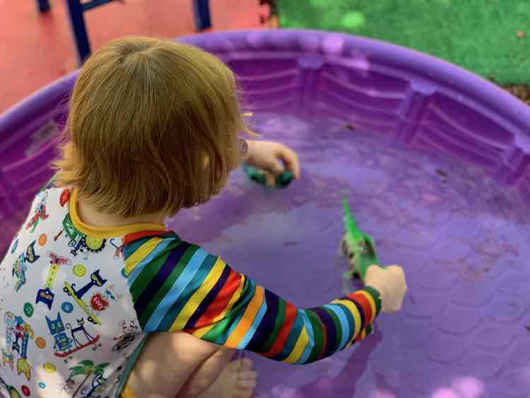 Playing with dinosaurs in the pool while wearing Pete the Cat.