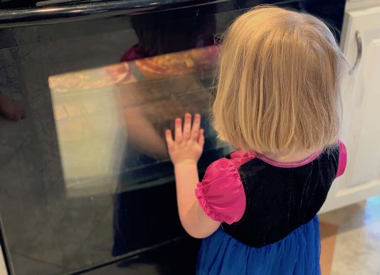 Ada on her knees in front of the lit up oven entranced at the contents inside.