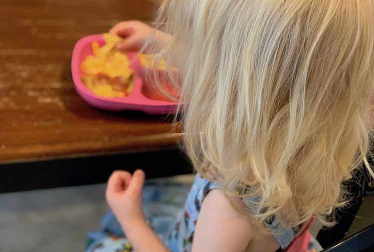 View from behind Zoey as she eats the leftover cheese and pineapple from her plate of pizza toppings.