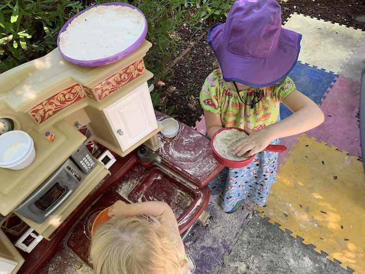 Zoey making something in an orange bucket, Ada mixing oobleck sand and real sand together, and pressed down oobleck sand sunning itself on top of the kitchen set.