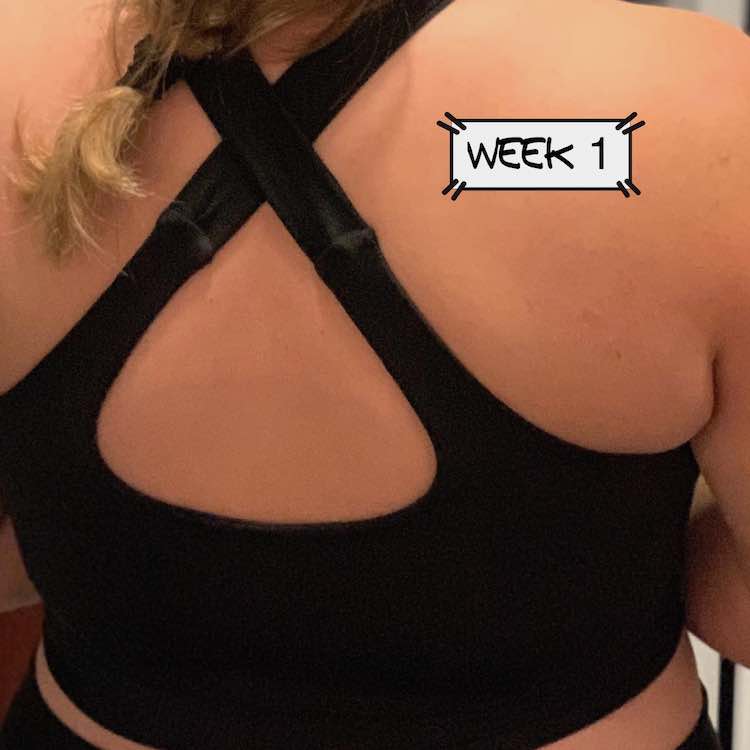 Back of my black crisscross strapped bra. The label "week 1" has been added to the back of my shoulder.