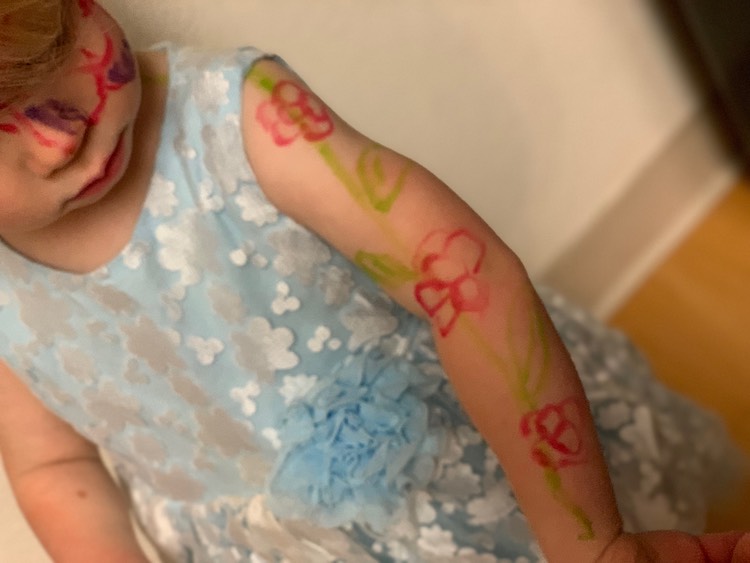 Zoey wearing a blue dress with white flowers. There's a green stem with pink flowers going up her arm and surrounding her eye.