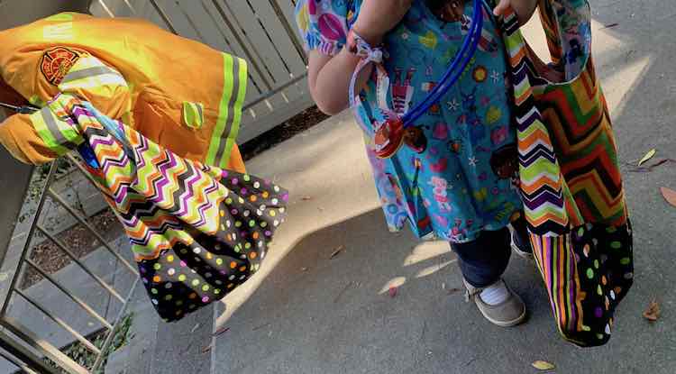 Ada in her firefighter costume carrying her halloween bag on the left and Zoey facing the camera on the right. She's wearing a Doc McStuffins top, carrying her Halloween bag, and is wearing a Doc McStuffins ribbon around her wrist while having a stethoscope around her neck.