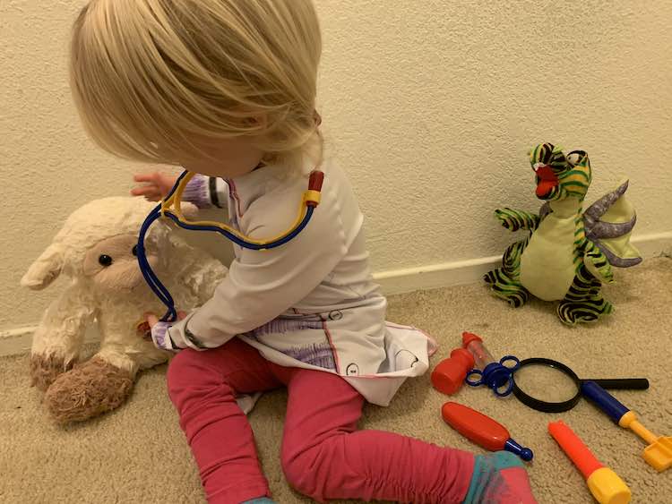 Quick photo before leaving. Zoey siting on the ground with the dragon stuffy and her tools beside her. She's leaning over the lamb toy on the other side of her while checking it's heart rate with her stethoscope.