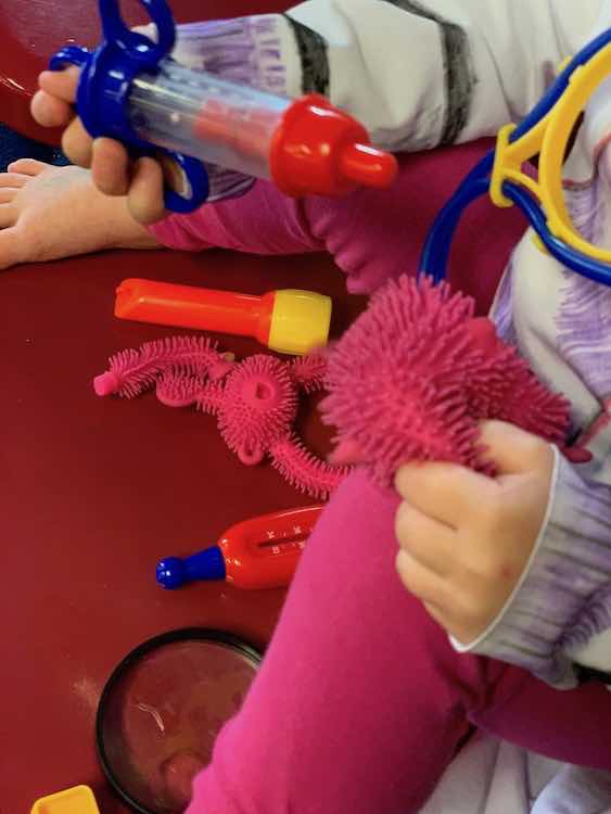 Again sitting on a red chair with her patients and doctor tools. This time shes about to give a needle to the broken squeeze toy.