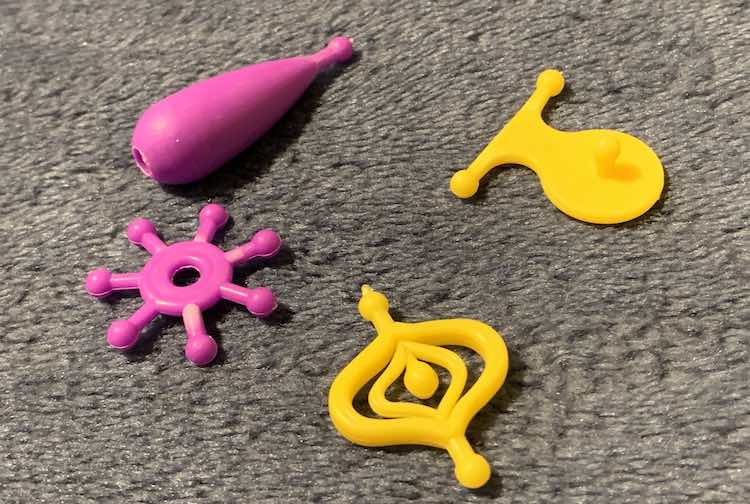 The four potential beads I could see using to make the unicorn pendant. Top left is more a cylindrical teardrop shape, top right is a pendant with a nubbin and two attachment points making it the perfect pendant, bottom left is a circle with spokes sticking outward from it, and bottom right is a oval shaped decorative piece with two connection points on either side.