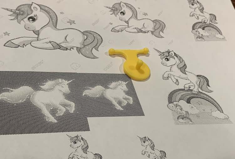 Paper printed with grayscale unicorns. The yellow pop snap bead pendant lays in the center to help compare sizes.