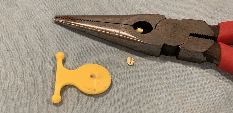 Yellow pendant with the nubbin cut out. A piece of the nubbin lies within the cutting pliers while another piece lies between the two.