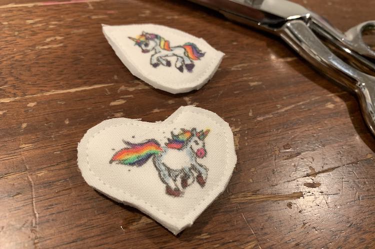 The two unicorns all cut out. The heart is in the foreground, while the teardrop shaped one is in the background. Behind both are shown my scissors. 