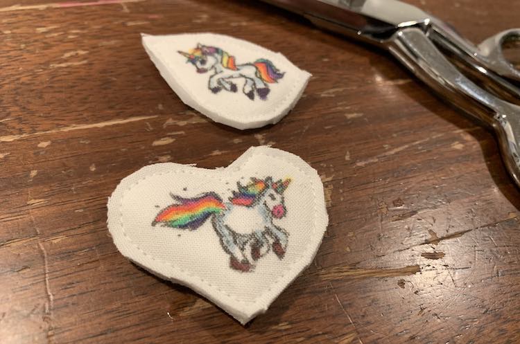 The two unicorns all cut out. The heart is in the foreground, while the teardrop shaped one is in the background. Behind both are shown my scissors.