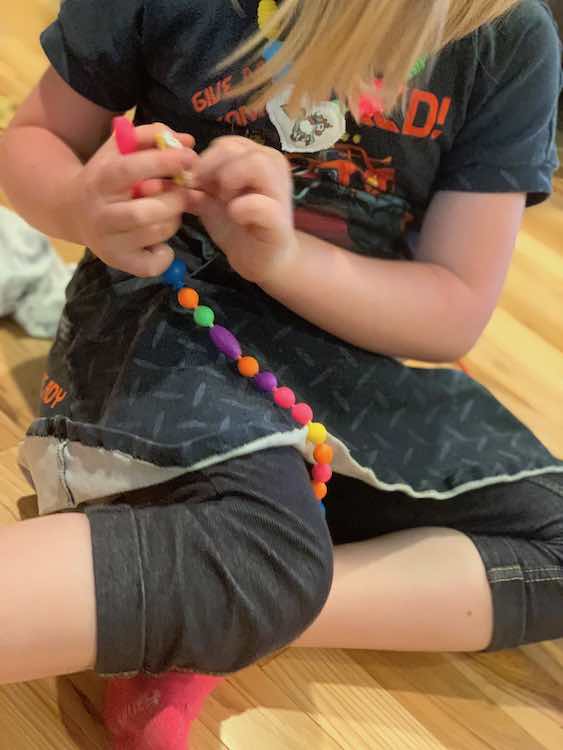 Ada sitting down and about to add the other pendant to a newly made strand of pop snap beads.