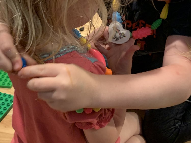 Ada putting Zoey's new necklace on her while Zoey examines Ada's unicorn on her necklace.