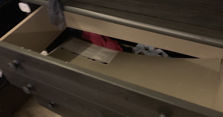 Dresser drawer emptied and pulled out from the dresser. You can see the drawer bottom’s corner completely fallen into the clothing below. 