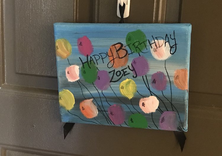 The finished canvas shown hanging in front of an outside door on a white command hook.