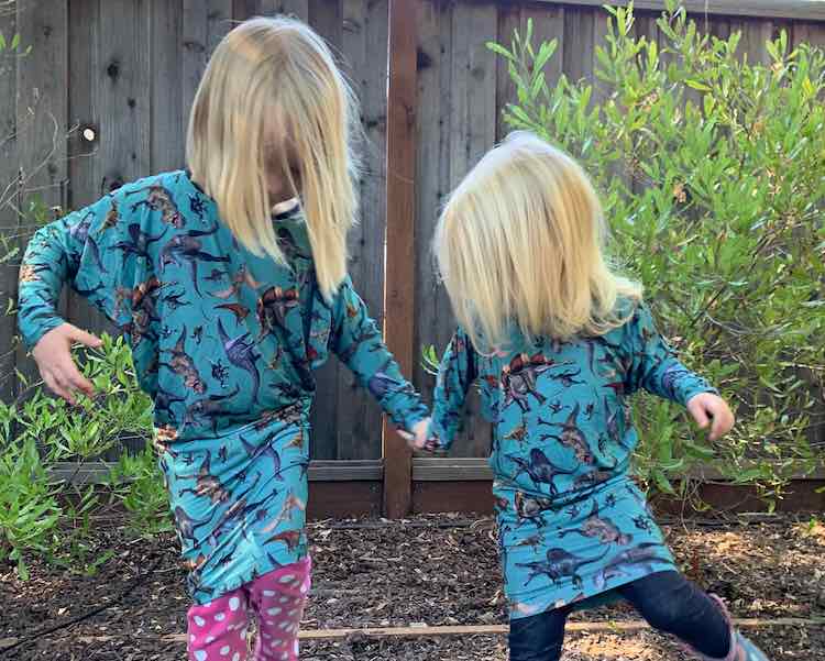 Sisters wearing their new dresses holding hands and trying to flamingo (balance while lifting a foot).