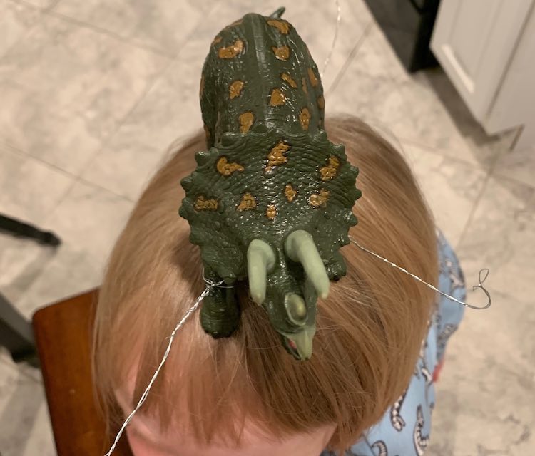 The dinosaur stands in all his plastic glory on Adas smooth hair. You can see two of the four wire offshoots ready to be attached.