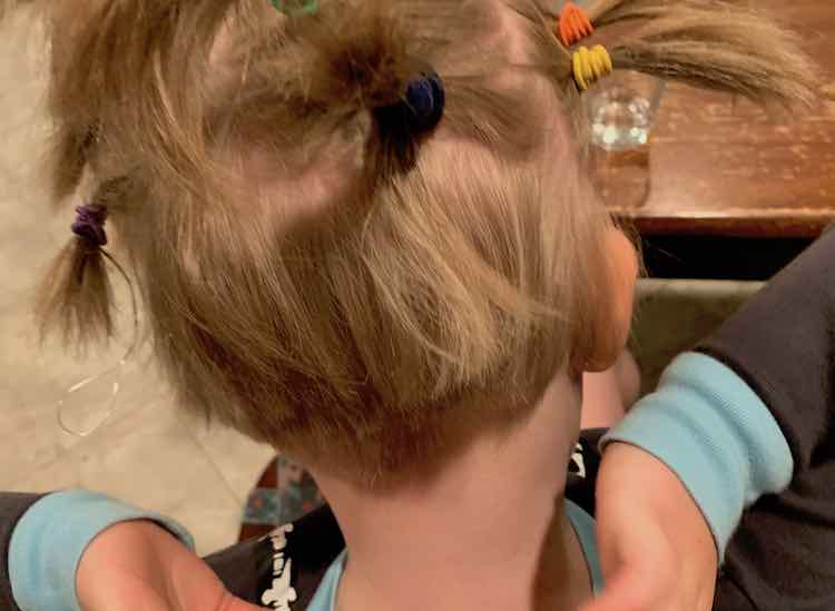 Back view of Ada's head after the ponytails were done being created. The top of her head shows several ponytails jutting out but the bottom shows short hair at the nape of her neck.