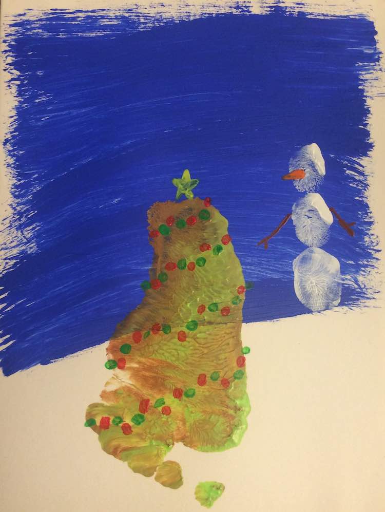 Closeup of a Christmas card showing a footprint tree adorned with angled rows of green and red dots and a yellow star sitting at the top. The snowman to the right had brown twig arms and a yellow triangle nose. 