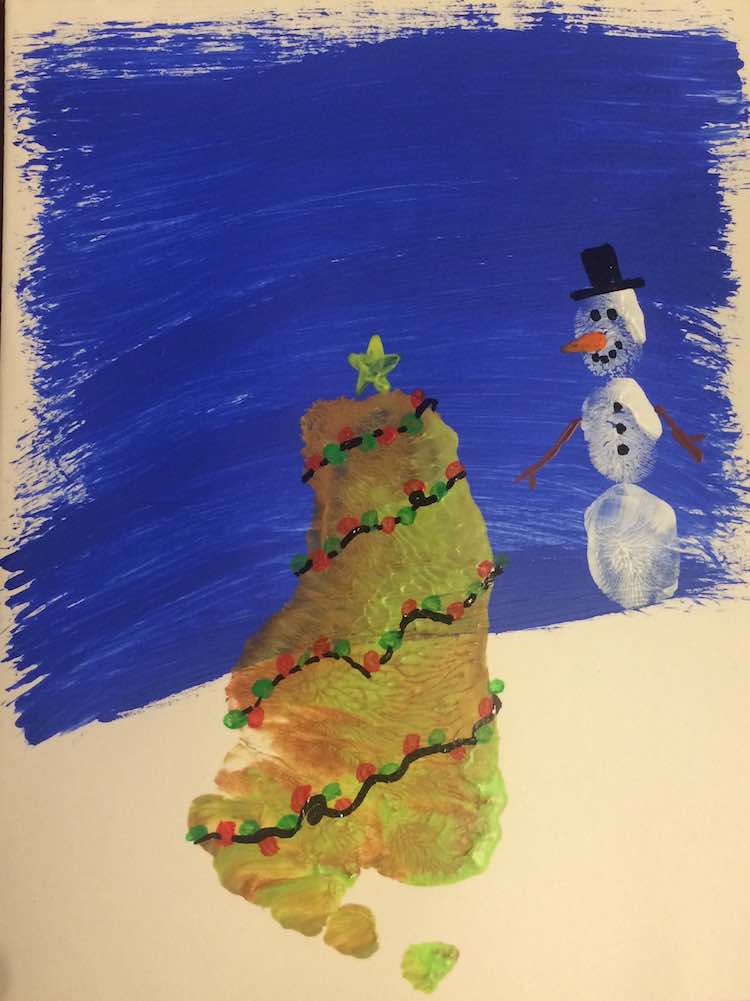 Finished Christmas tree and snowman. The tree has a yellow star at the top and is surrounded by a string of red and green Christmas lights. The snowman has a top hat, twig arms, carrot nose, coal face, and coal buttons.