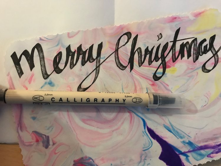"Merry Christmas" written across the top of the marbled paper with an opened blank card behind it. 