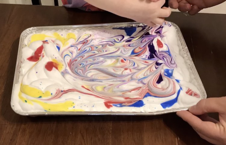 Ada marbling the shaving cream. The drops of watercolors on the left remain mostly unsmeared while the rest have been swirled.