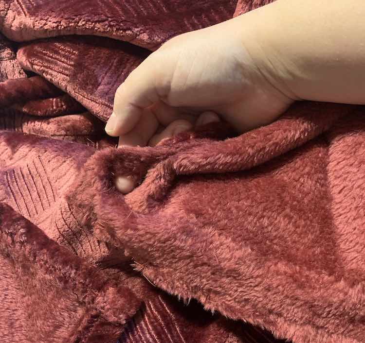 Reddish throw with a corner of it being held in my hands and a finger going through the hole in it. 