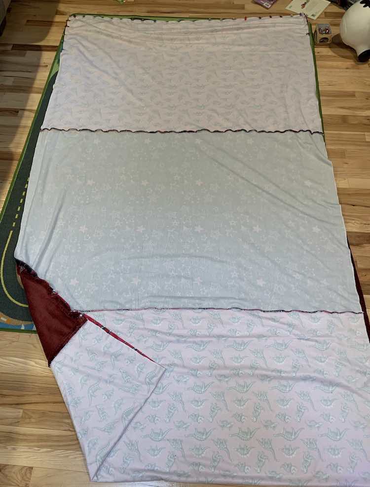 Photo looks down at the wrong side of the sewn together dinosaur and star fabric. The bottom of either fabric (show at the top) is clipped together while the sides are not yet. 