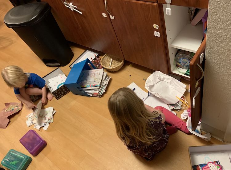 Kids on the floor going through their artwork with the cupboard door open.