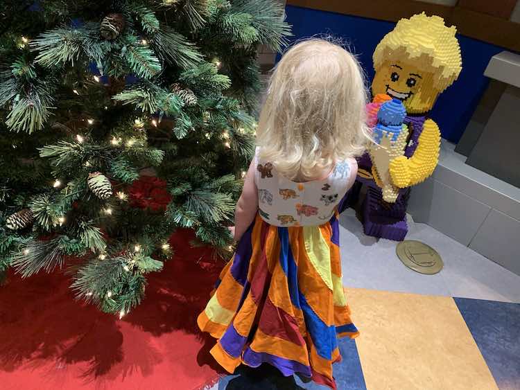 Zoey, wearing the dress, at LEGOLAND® standing in front of the Christmas tree looking at the LEGO® statue of the boy with his ice cream cone.