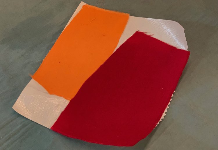 Photo showing two rectangular scraps of fabric, one orange and one red, attached to the shiny side of heat'n bond interfacing, 