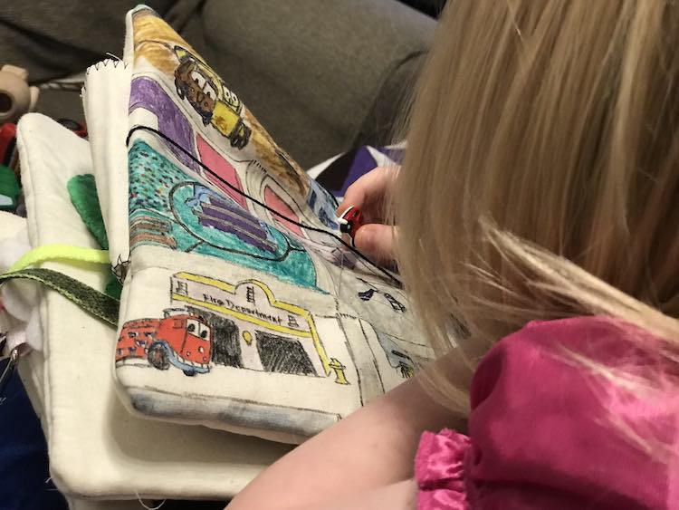 Back view of Ada playing with her new button quiet book page. Behind it you can see the shoelace from the shoe tying page and part of the green felt of the 'brush your teeth' crocodile. 