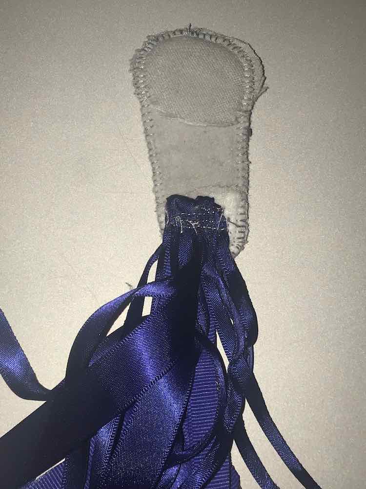 The underside of the faucet is shown which lets us see the extra interfacing at the top and bottom. The ribbons where folded in half with all of their ends going off the bottom (end) of the spout. The ribbons are sewn down multiple times along it's fold attaching it to the faucet.