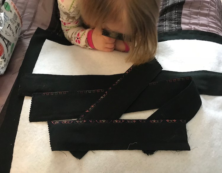 The four finished edges are laid overtop of the interfacing with the black fabric behind it. Ada's head is in view as she lays on her belly looking at the fabric with her magnifying glass. 
