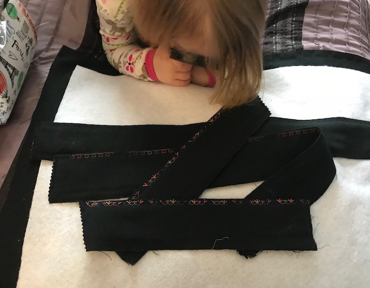 The four finished edges are laid overtop of the interfacing with the black fabric behind it. Ada's head is in view as she lays on her belly looking at the fabric with her magnifying glass.