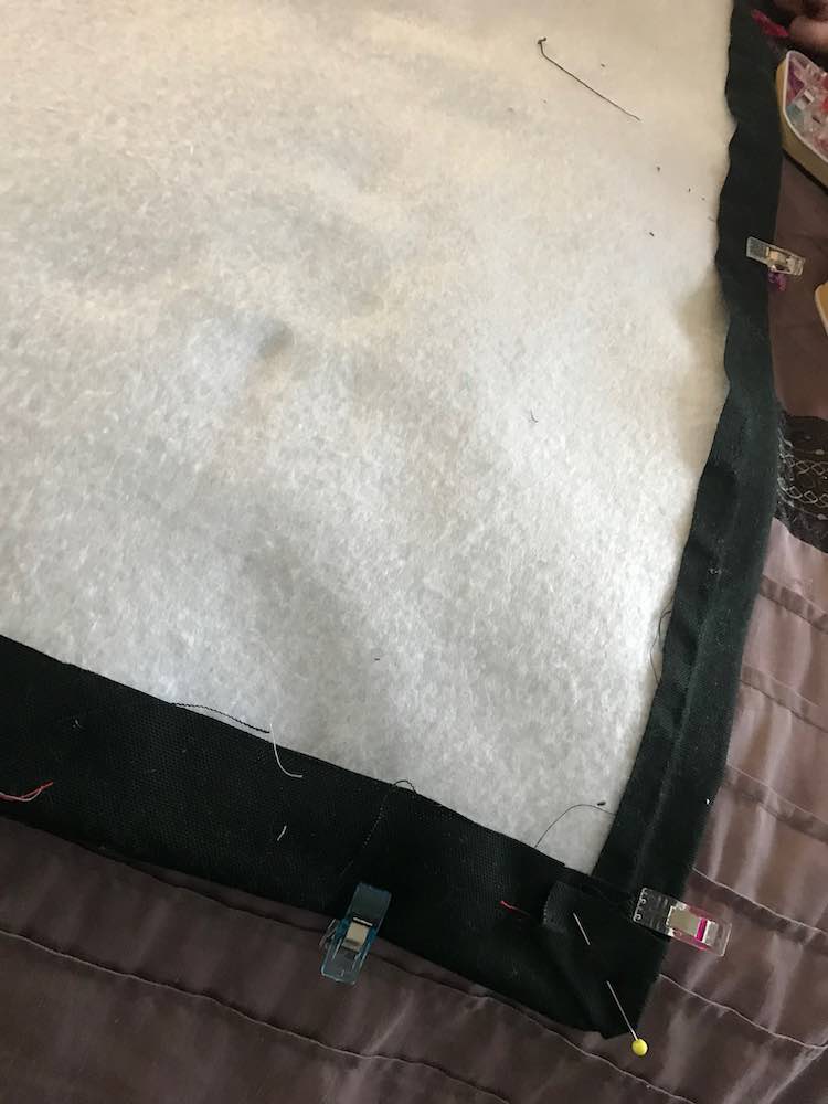 Shows the underside of the cover with the black woven fabric folded under to cover the edge of the fusible fleece. The sides are kept in place with sewing clips while the corner is pinned.