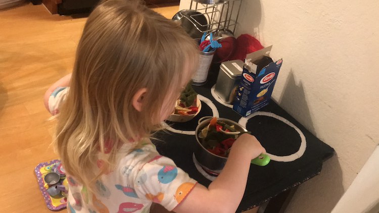 Back overview of Ada stirring up her concoction of pasta and tomatoes on the heated burner.