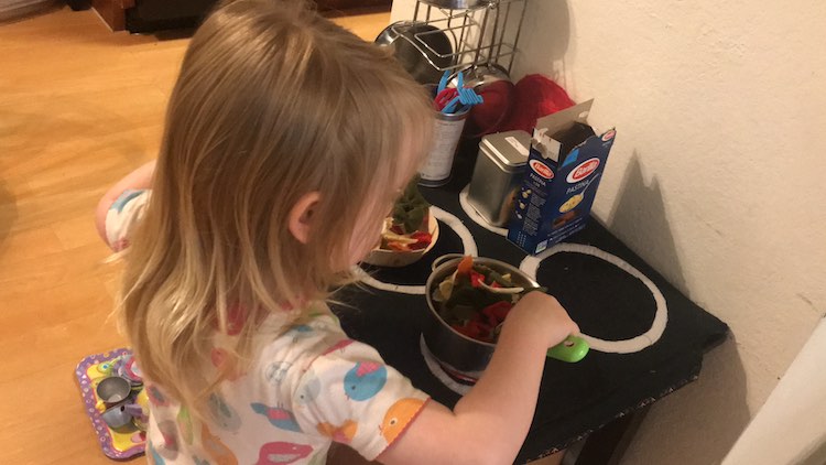 Back overview of Ada stirring up her concoction of pasta and tomatoes on the heated burner. 